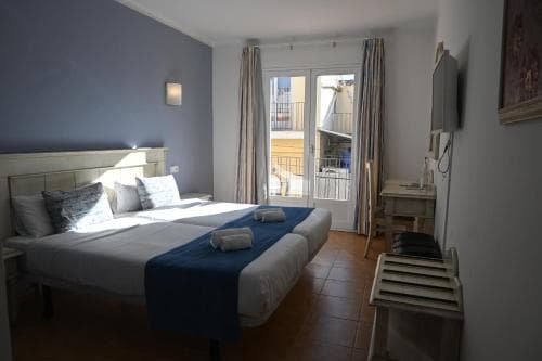 A cozy hotel room with a neatly made bed, blue accents, and a balcony view, exudes a serene atmosphere ideal for travelers seeking relaxation.