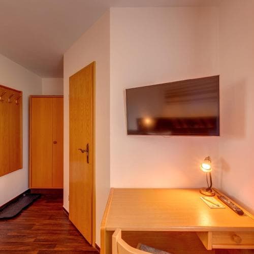 A cozy hotel room corner features a wooden desk with a lamp and TV mounted on the wall, creating a warm and inviting atmosphere ideal for travelers seeking comfort and functionality.
