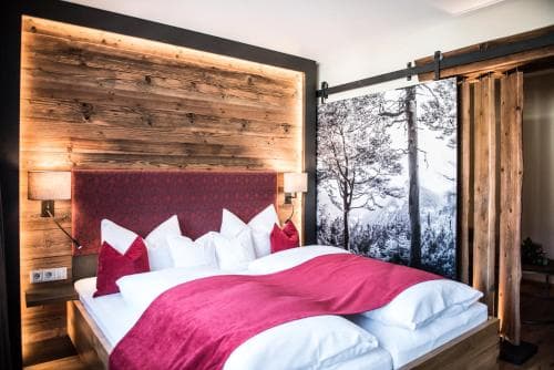 A cozy hotel room with a rustic wooden interior, a plush bed adorned with red accents, and a serene snowy forest mural, ideal for travelers seeking relaxation in a mountain retreat.