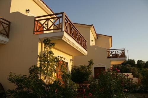 A serene Mediterranean villa with wooden balconies and lush greenery offers a tranquil retreat for travelers seeking relaxation in a picturesque coastal setting.