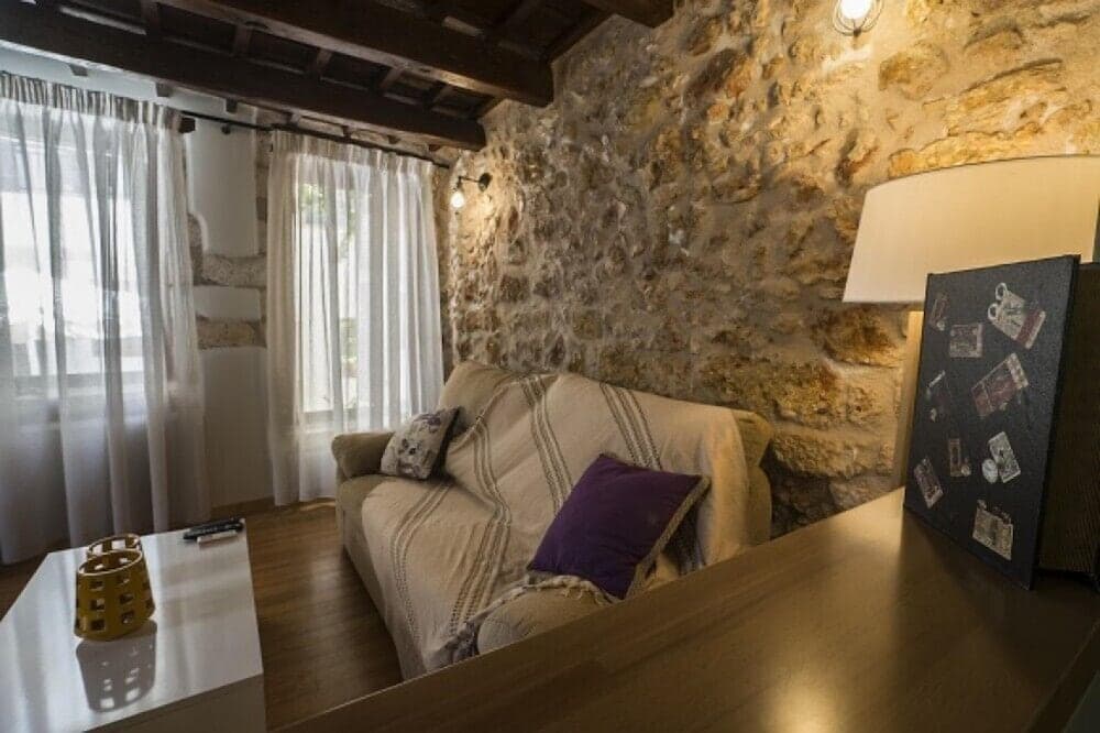 A cozy living room with rustic stone walls, wooden beams, and modern furnishings creates an inviting atmosphere perfect for travelers seeking a charming and comfortable retreat.