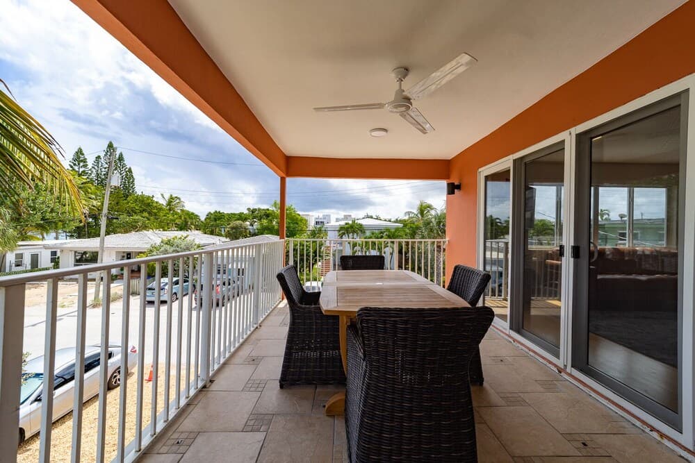A cozy balcony with a wicker dining set overlooks a tropical street lined with palm trees, perfect for travelers seeking a relaxing retreat in a sunny destination.