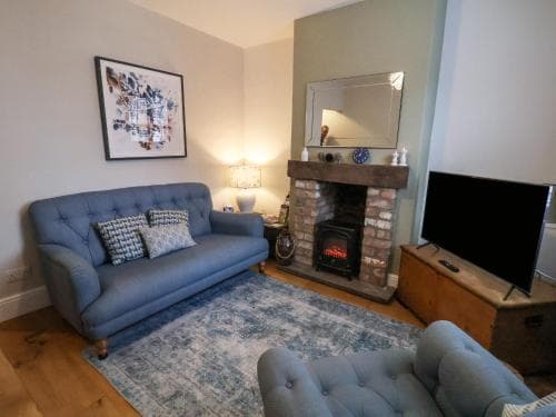 A cozy living room with a blue tufted sofa, brick fireplace, and warm lighting creates an inviting atmosphere, perfect for travelers seeking comfort in a homey vacation rental.