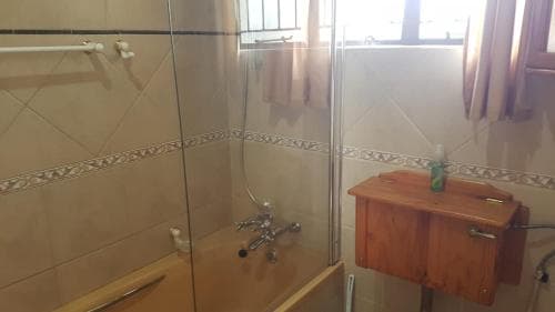 A cozy bathroom with beige tiled walls, a glass shower enclosure, wooden vanity, and natural light from a window creates a warm and inviting atmosphere, ideal for travelers seeking comfort in their accommodations.