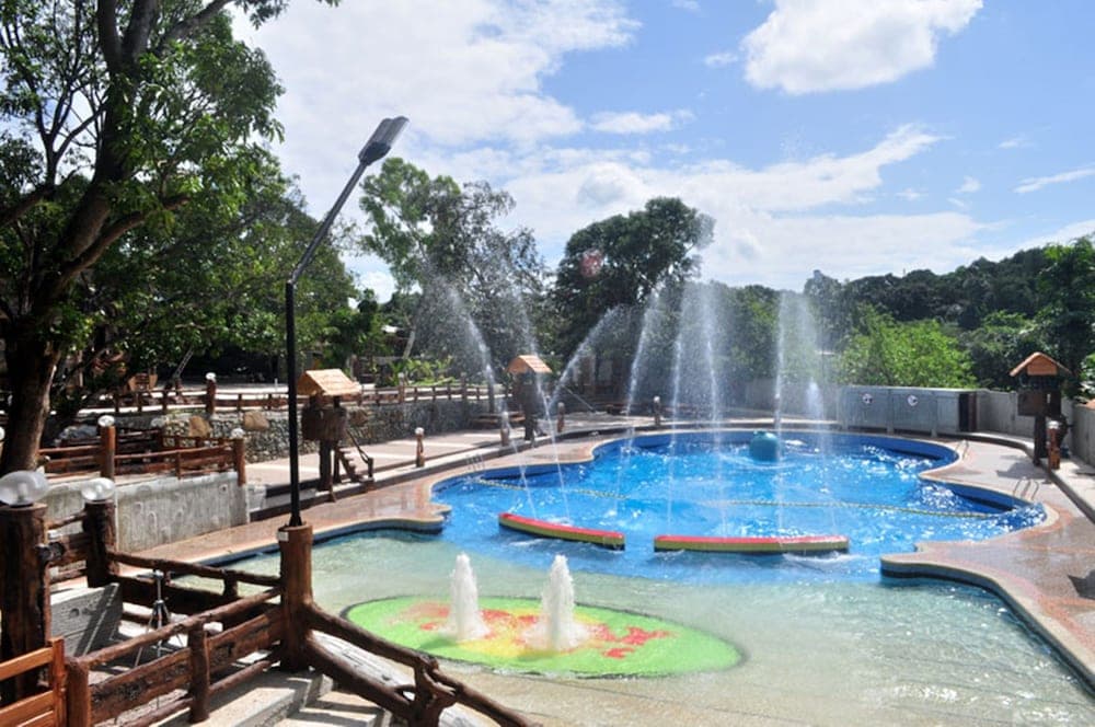 A vibrant outdoor water park features playful fountains, colorful platforms, and lush greenery under a sunny sky, ideal for family fun and relaxation.