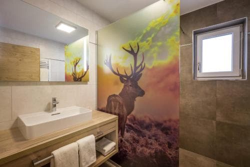 A modern bathroom features a striking deer mural under a sunset sky, complemented by wooden accents and a sleek sink, creating a serene and artistic atmosphere ideal for eco-luxury retreats.
