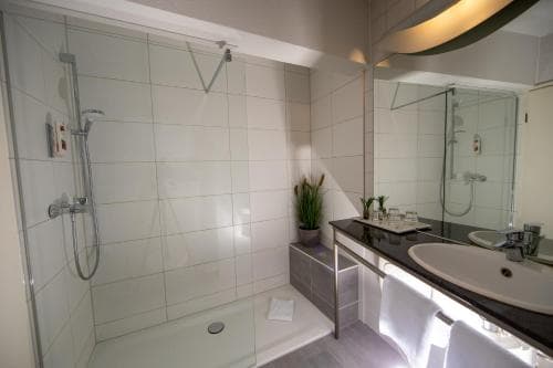 A modern hotel bathroom features a sleek walk-in shower, a black countertop vanity with dual sinks, and a minimalist design, ideal for travelers seeking comfort and cleanliness.