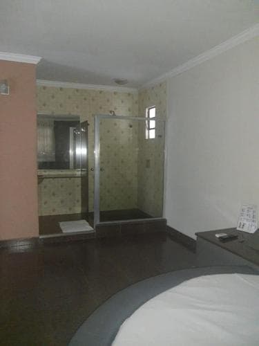 A cozy hotel room features a compact bathroom with a glass shower enclosure, patterned wallpaper, and a neatly made bed, ideal for travelers seeking comfort in a modest setting.