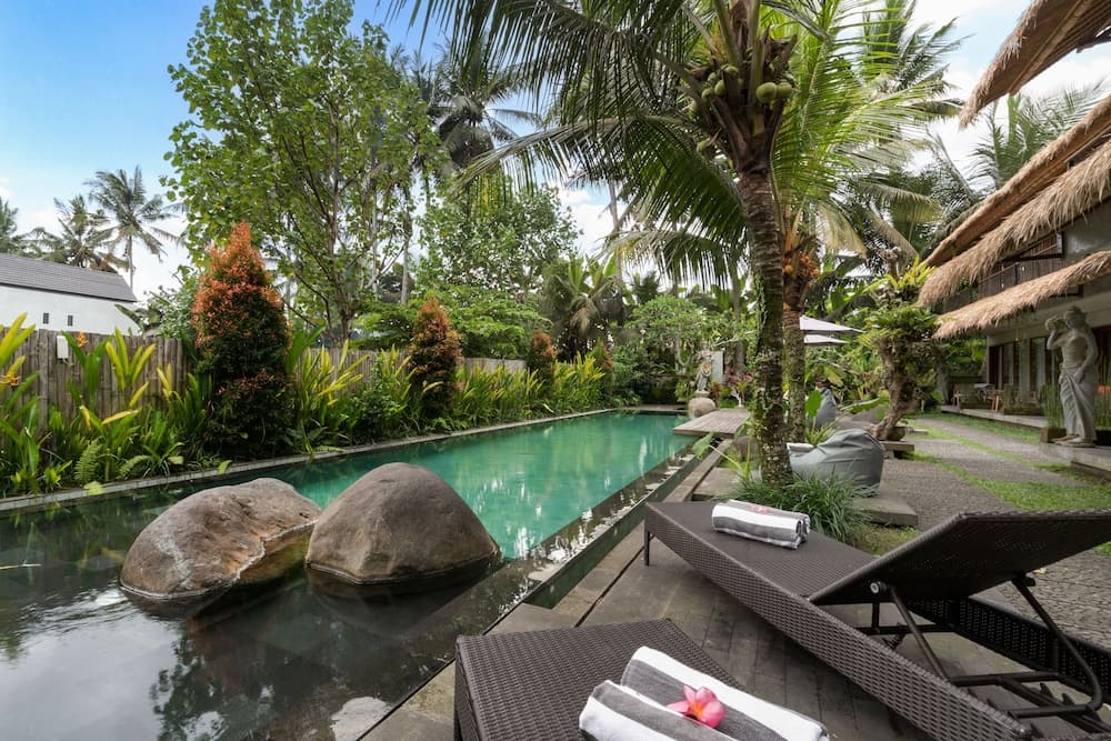 A serene tropical resort features a tranquil pool surrounded by lush greenery, palm trees, and thatched-roof structures, ideal for relaxation and vacation photography.