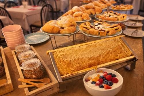 A cozy breakfast buffet scene featuring fresh pastries, honeycomb, yogurt with berries, and granola, set in a warm, inviting dining area perfect for travelers seeking a delightful morning start.