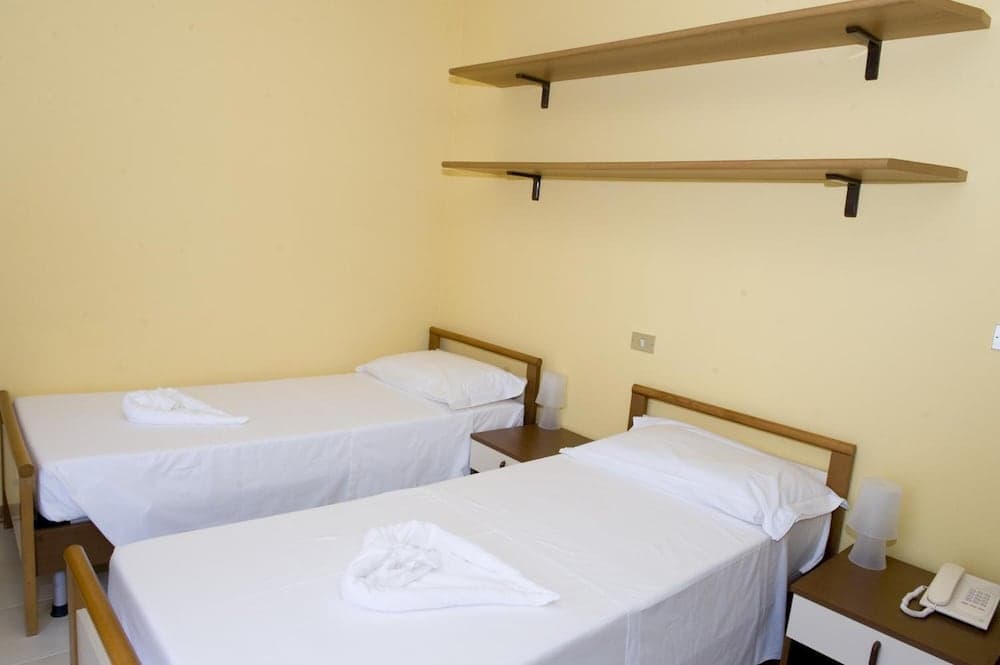 A cozy hostel room with two neatly made beds, wooden shelves, and minimal decor offers a simple yet inviting space for budget travelers seeking comfort.