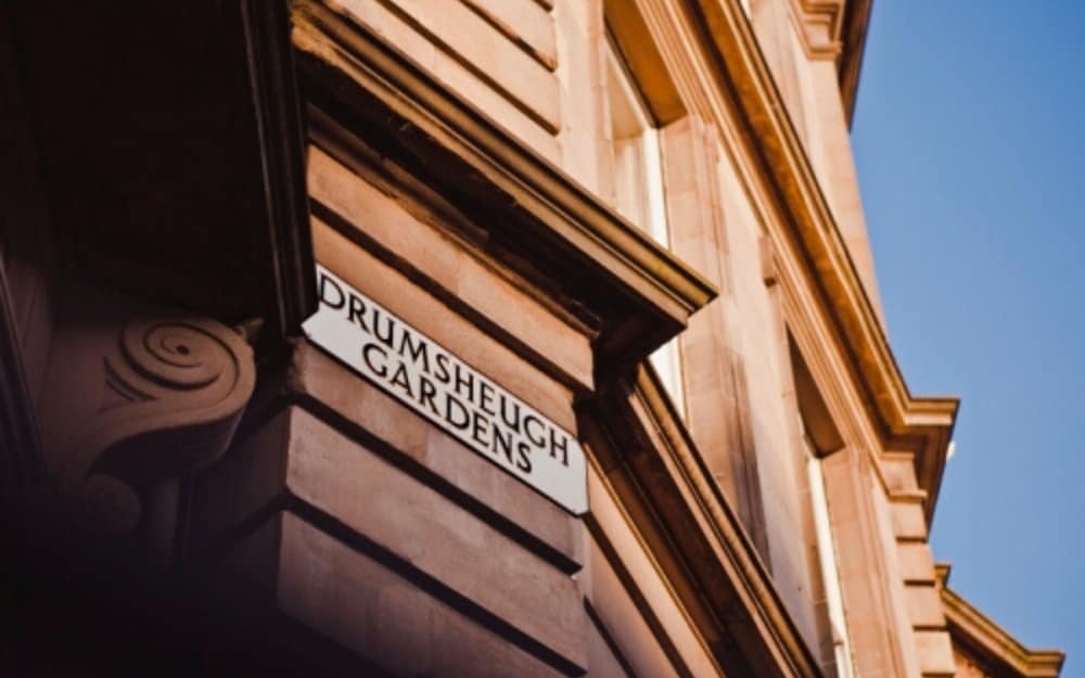 A historic building corner with a "Drumsheugh Gardens" street sign bathed in sunlight under a clear blue sky, evoking a serene urban exploration vibe ideal for cityscape photography enthusiasts.
