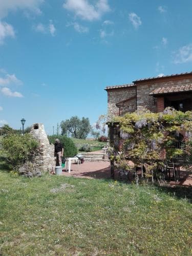 A serene countryside retreat features a rustic stone building adorned with climbing flowers, a quaint garden path, and a clear blue sky, ideal for a peaceful vacation escape.