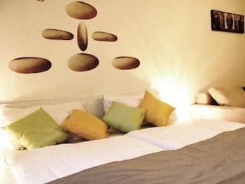 A cozy bedroom with a bed adorned in soft green and yellow pillows, illuminated by warm ambient lighting, features a wall decorated with stone-like decals, creating a serene and inviting atmosphere ideal for relaxation and restful sleep.