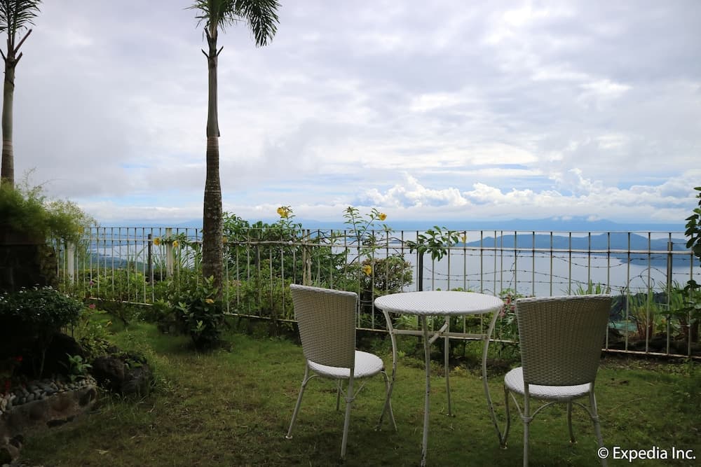 A serene outdoor patio with white wicker furniture overlooks a tranquil coastal landscape under a partly cloudy sky, ideal for travelers seeking relaxation and scenic views.