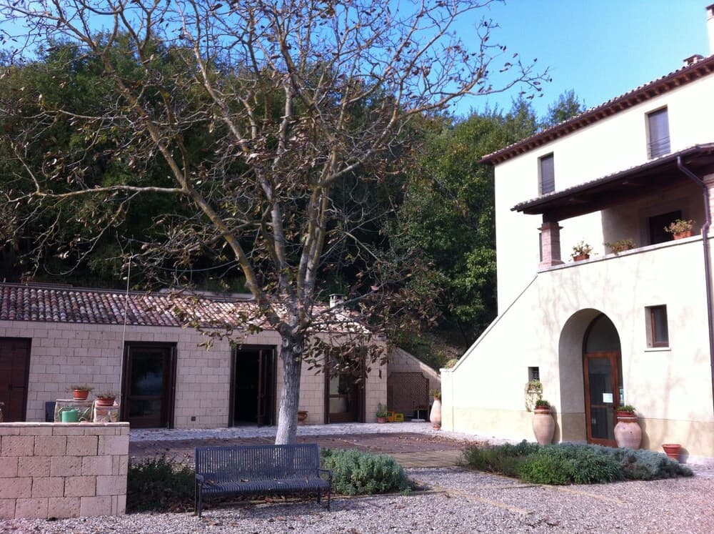 A serene courtyard with rustic stone buildings, potted plants, and a leafy tree offers a tranquil retreat ideal for countryside relaxation and photography.