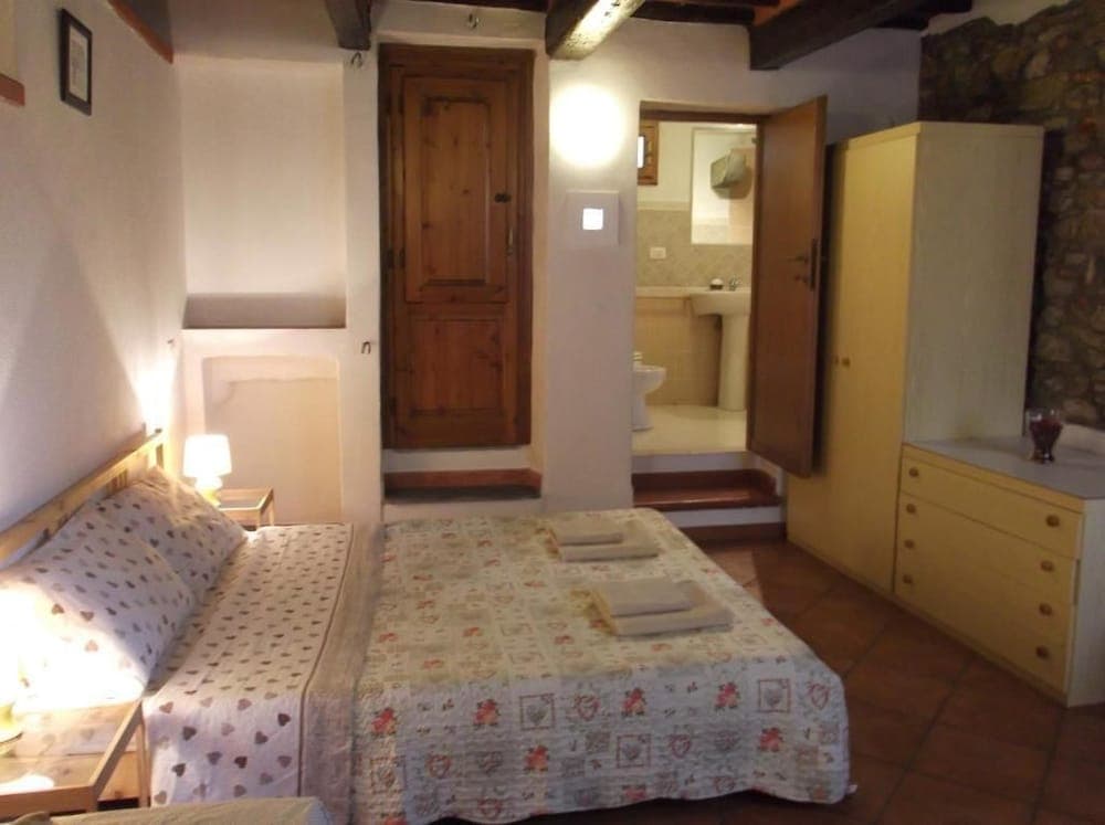 A cozy bedroom with rustic charm features a neatly made bed, wooden beams, stone walls, and an en-suite bathroom, ideal for travelers seeking a quaint and comfortable stay in a traditional setting.