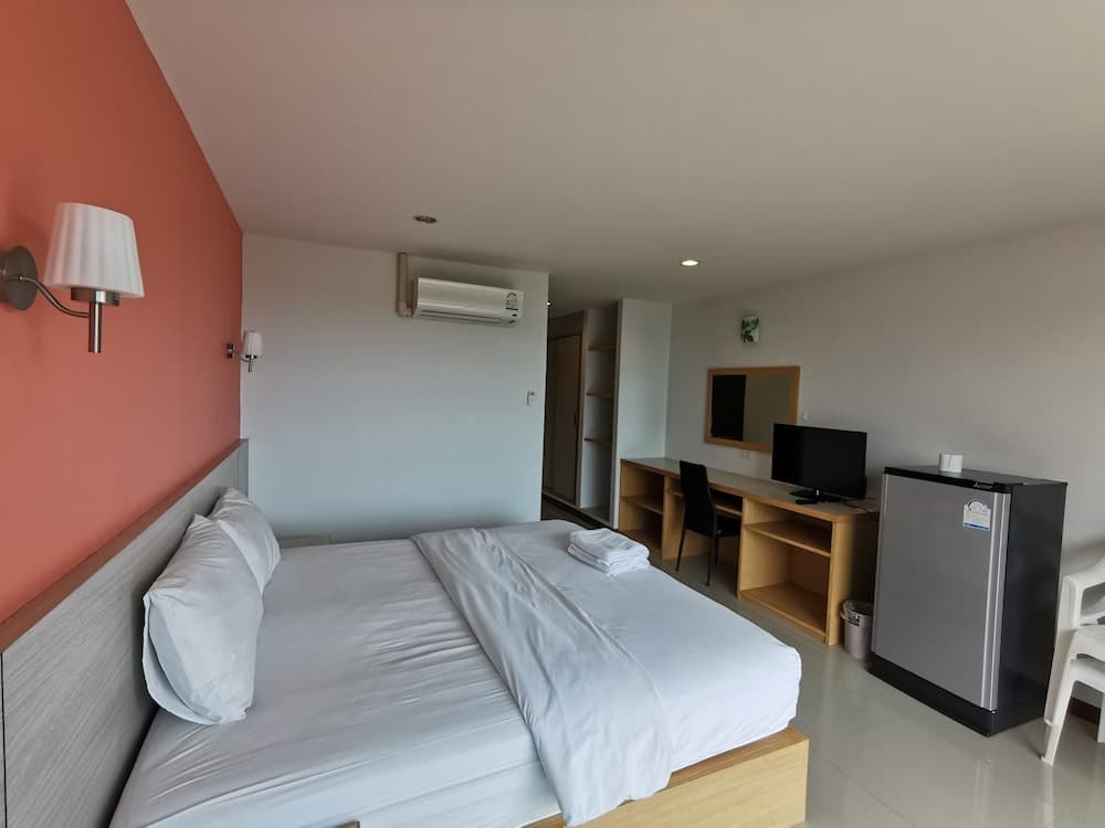 A cozy hotel room features a neatly made bed against an orange accent wall, a wooden desk with a TV, a mini-fridge, and a modern ambiance ideal for travelers seeking comfort and convenience.
