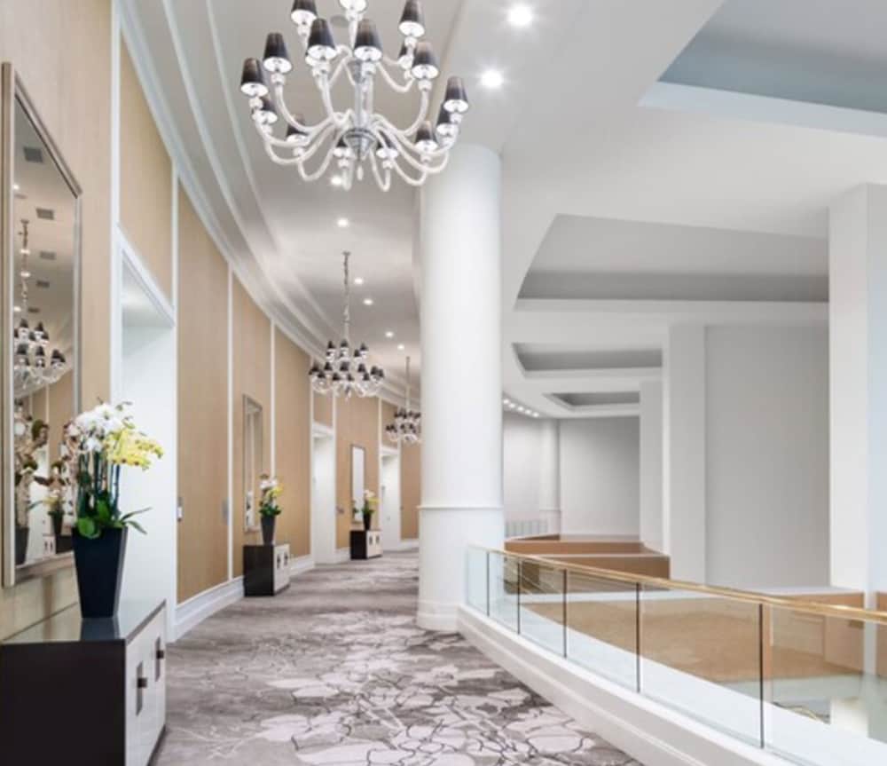 A luxurious hotel corridor features elegant chandeliers, plush carpeting, and modern decor, creating an inviting atmosphere ideal for travelers seeking upscale accommodations.