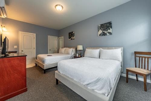 A cozy hotel room features two neatly made beds under soft lighting, with a wooden desk, chair, and framed artwork creating a welcoming atmosphere ideal for travelers seeking comfort and relaxation.