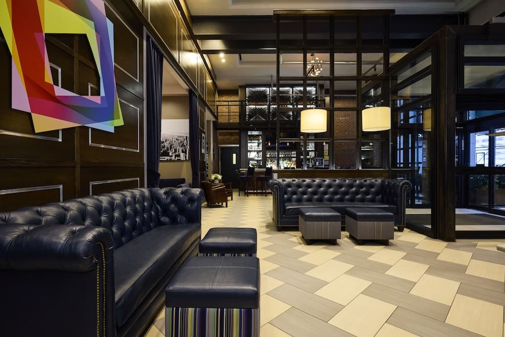 A cozy hotel lobby features plush leather couches, vibrant artwork, and a modern tiled floor, creating an inviting atmosphere ideal for travelers seeking relaxation and style.
