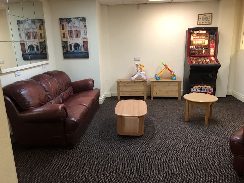 A cozy indoor lounge features a plush leather sofa, wooden tables, colorful children's toys, and a Monopoly arcade machine, creating a relaxed family-friendly atmosphere ideal for travelers seeking leisure and entertainment.