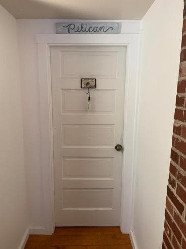 A cozy indoor hallway features a white door labeled "Pelican," set against a brick wall, creating an inviting atmosphere ideal for travelers seeking a charming accommodation entrance.