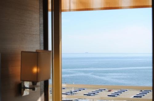A serene hotel room with a warm lamp overlooks a tranquil beach scene through large windows, ideal for travelers seeking relaxation by the sea.