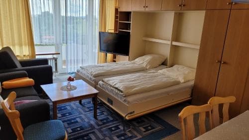 A cozy hotel room with twin beds, a flat-screen TV, and a balcony view through sheer curtains, ideal for travelers seeking comfort and relaxation.