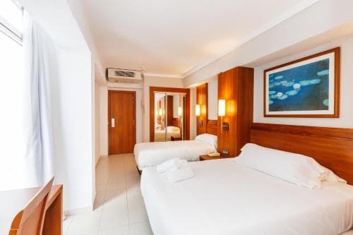 A cozy hotel room features two neatly made beds, warm wooden furnishings, and a serene water lily painting, creating an inviting atmosphere ideal for travelers seeking comfort and relaxation.