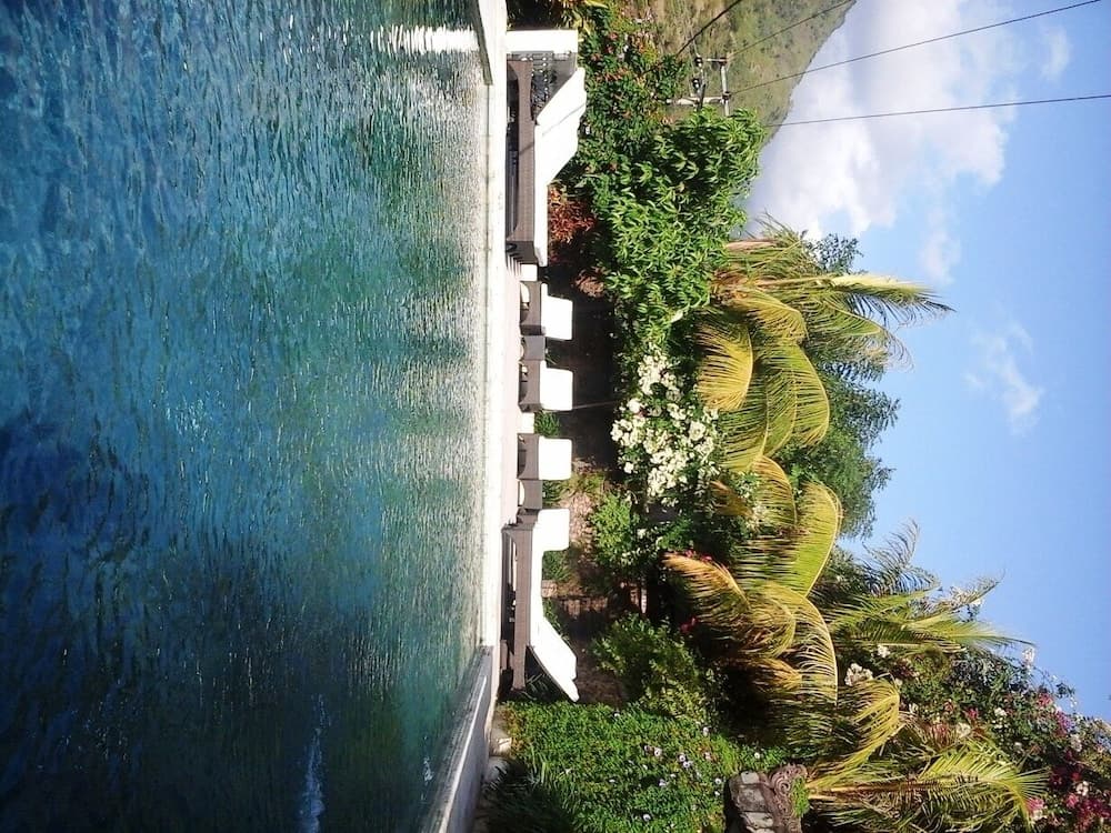 A serene tropical resort poolside scene features lush greenery, palm trees, and white lounge chairs under a clear blue sky, ideal for vacation relaxation.