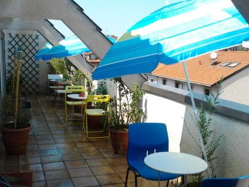 A cozy outdoor terrace with vibrant blue umbrellas, colorful chairs, and potted plants creates a relaxed atmosphere ideal for travelers seeking a peaceful dining or lounging spot.