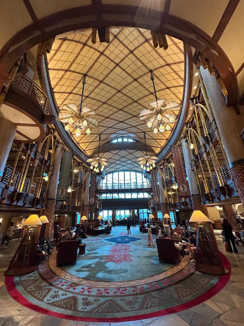 A grand, warmly lit lobby with intricate rugs, soaring arched ceilings, and decorative banners creates an inviting atmosphere at the Disney Explorers Lodge on Lantau Island, perfect for family vacations seeking adventure and luxury.