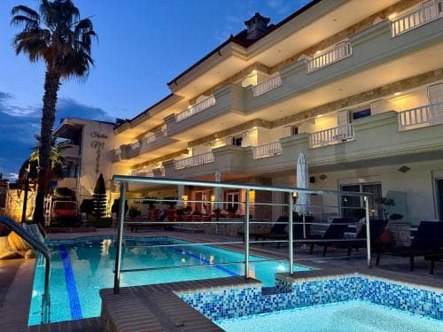 A serene evening at a luxurious hotel features a glowing poolside area with lounge chairs, palm trees, and balconied rooms, ideal for travelers seeking relaxation and comfort.
