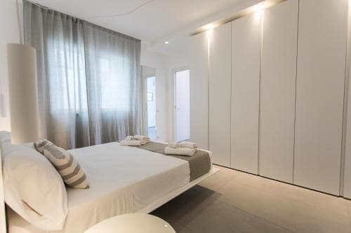 A serene minimalist bedroom features a sleek white bed, soft gray curtains, and modern built-in wardrobes, ideal for travelers seeking a tranquil urban retreat.