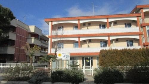 A sunny day highlights a charming multi-story apartment complex with balconies, surrounded by lush greenery, ideal for travelers seeking comfortable coastal accommodations.