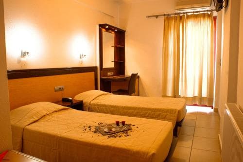A cozy hotel room with two neatly made beds adorned with decorative petals, warm lighting, a wooden desk, and a window with curtains, ideal for travelers seeking comfort and relaxation.
