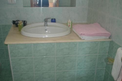 A cozy bathroom with light green tiled walls features a white sink, neatly folded pink towels, and toiletries, ideal for travelers seeking cleanliness and comfort in accommodations.
