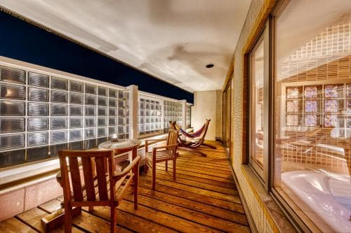 A serene indoor relaxation area features wooden flooring, glass block walls, cozy chairs, and a hammock, ideal for travelers seeking a tranquil spa retreat experience.