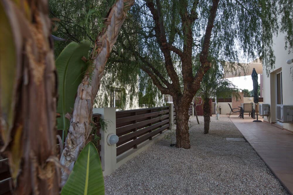 A serene courtyard pathway lined with gravel, lush trees, and wooden railings offers a tranquil retreat for travelers seeking relaxation in a private villa setting.