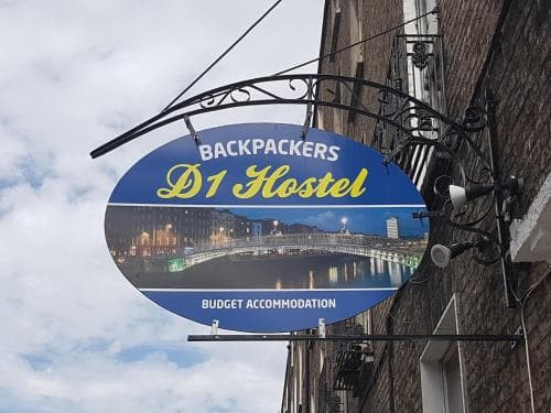 A vibrant signboard for the D1 Hostel, offering budget accommodation for backpackers, hangs against a brick building under a partly cloudy sky, ideal for travelers seeking affordable lodging in an urban setting.