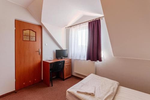 A cozy attic room with slanted ceilings features a neatly made bed, a desk with a TV, and a wooden door, ideal for travelers seeking a quiet and comfortable stay in budget-friendly accommodations.