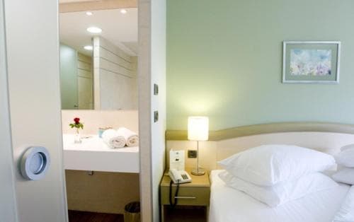 A cozy hotel room with soft lighting, a neatly made bed, and an adjacent bathroom featuring a sink with a vase of flowers, ideal for travelers seeking comfort and relaxation.