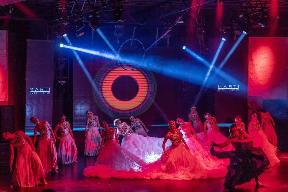 A vibrant stage performance featuring dancers in flowing costumes under dramatic red and blue lighting, ideal for cultural event enthusiasts seeking dynamic theatrical experiences.