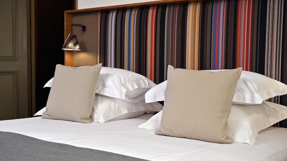 A cozy hotel room features a neatly made bed with white linens and beige pillows against a vibrant striped headboard, creating a warm and inviting atmosphere ideal for travelers seeking comfort.