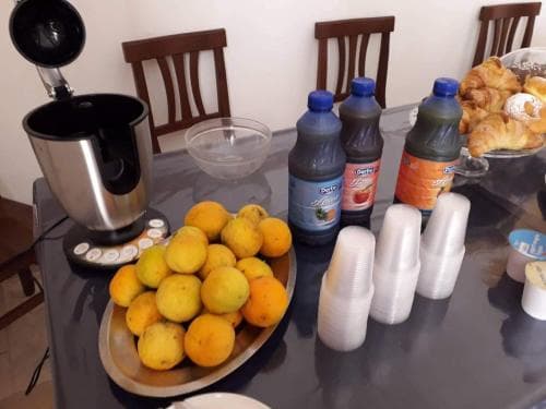 A cozy kitchen table set with fresh oranges, juice bottles, stacked cups, pastries, and a blender invites travelers to enjoy a homemade breakfast or brunch experience.