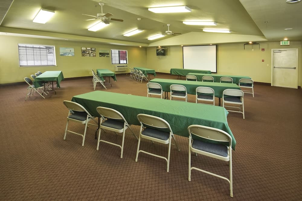 A well-lit conference room with green tablecloths, white chairs, and a projector screen creates an inviting atmosphere for business meetings or educational workshops.
