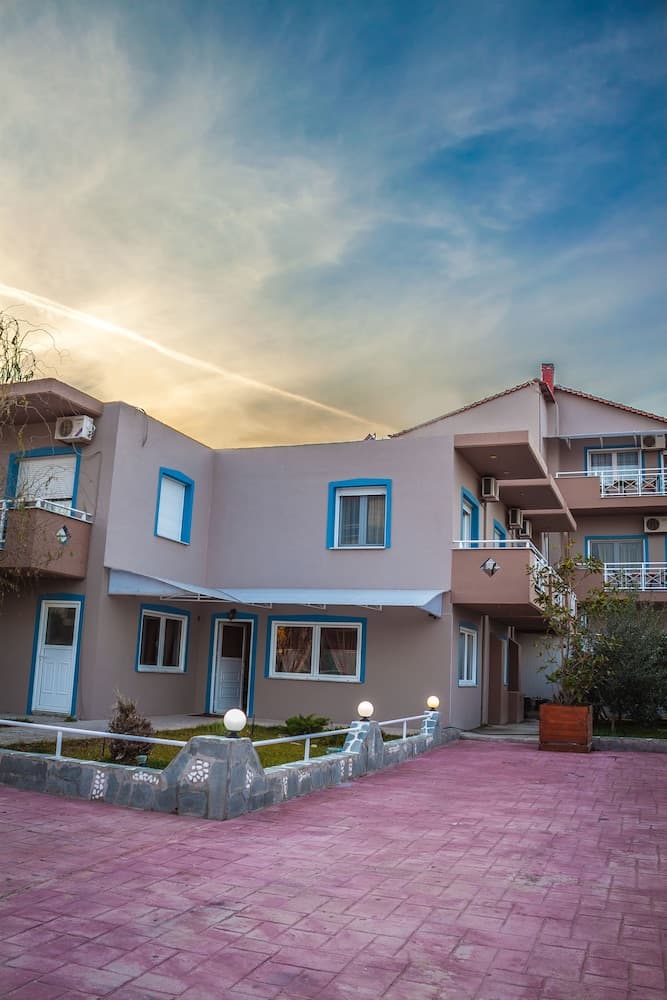 A serene residential complex with pastel-colored buildings, blue-trimmed windows, and a pink-tiled courtyard under a tranquil sunset sky, ideal for family vacations or long-term stays.