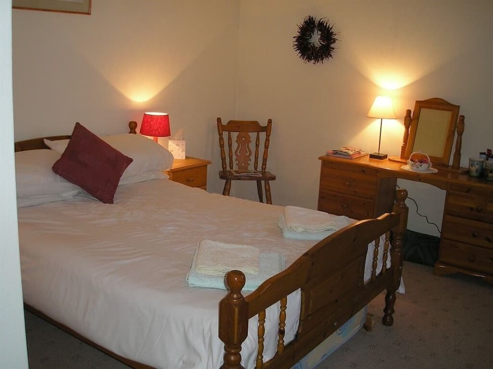 A cozy bedroom with warm lighting, wooden furniture, neatly folded towels on the bed, and a festive wreath creates an inviting atmosphere ideal for a relaxing getaway.