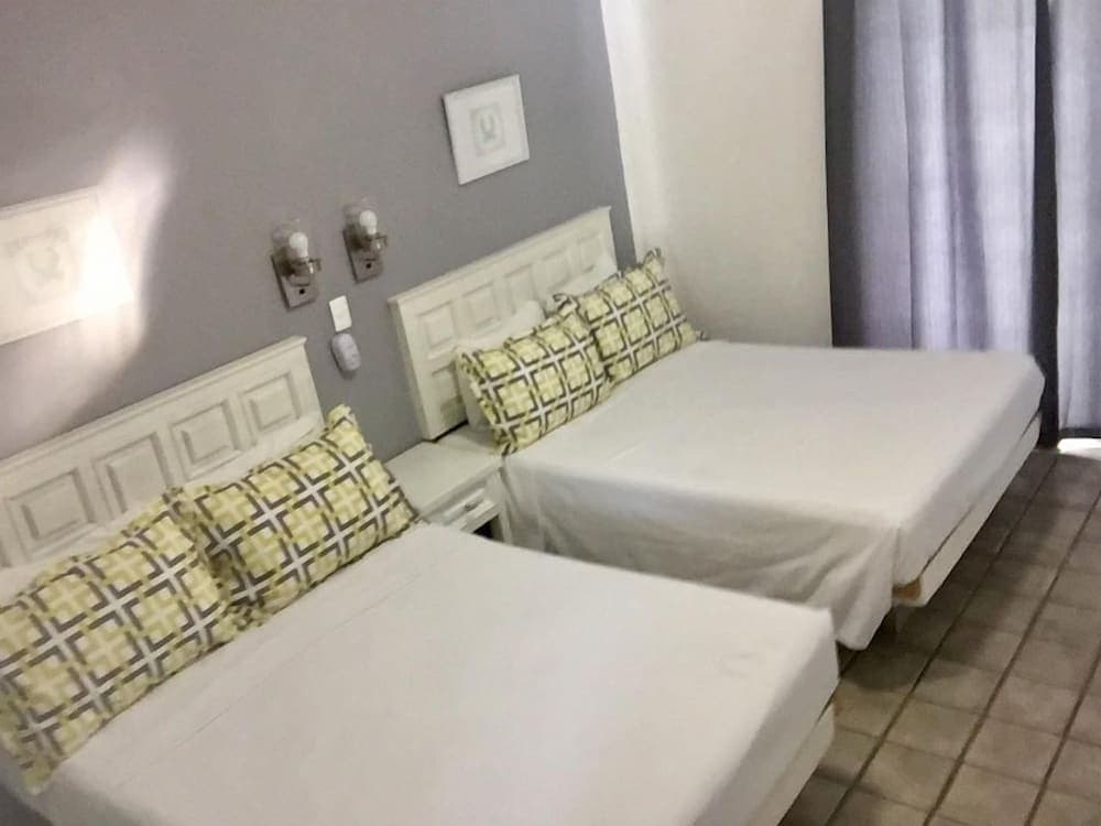 A cozy hotel room features two neatly made beds with white linens and patterned pillows, set against soft gray walls with wall-mounted lamps, ideal for travelers seeking comfort and simplicity.